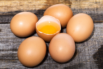 Whole and broken raw brown eggs on wooden table