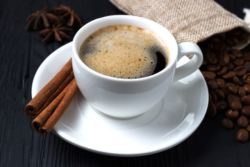 Coffee with cinnamon and anise on a black background and a bag of coffee beans