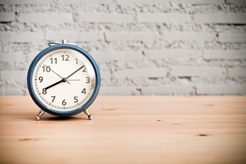 vintage alarm clock on the wooden table on brick wall background