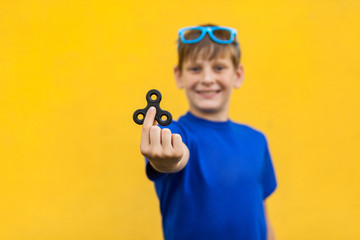 Young beautiful happy boy with freckles blue t-shirt holding fidget spinner on yellow background..