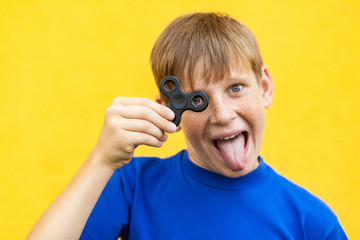 Young beautiful happy boy with freckles blue t-shirt holding fidget spinner on yellow background...