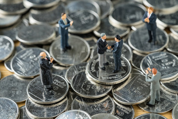 Miniature people: small figure businessmen handshaking and others clapping on stack of coin as money and financial agreement concept