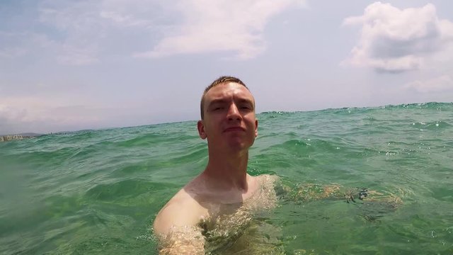 Man swims in the sea (he holds a gopro camera in his hand) 