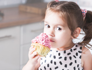 Cute little girl holding birthday cupcakes in kitchen. Festive and holiday concept