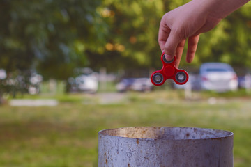 Closeup of a young caucasian man throwing a red fidget spinner in a garbage can on the background of nature.
