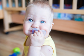 Portrait of funny baby with blue eyes and a pacifier in his mouth.