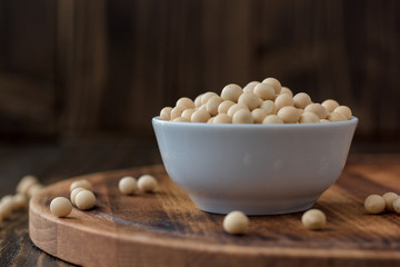 Organic soybeans at white ceramic bowl over wooden table.