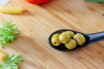 Green olives on black spoon over brown kitchen board.
