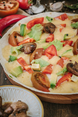 Vegetarian home made pizza with mushrooms and vegetables over wooden table, surrounded by ingredients