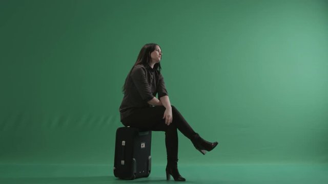 Young caucasian woman sitting on a suitcase and thinking