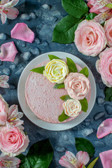 Frozen pink cake on a plate, decorated with roses from cream and mint leaves. Vertical photo. The dish is decorated with fresh flowers and ice.