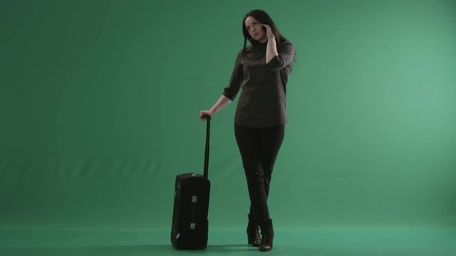 Young woman with a wheeled suitcase speaking on a cellphone