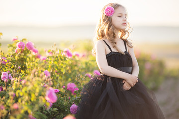 Fototapeta na wymiar Portrait of beautiful little girl is wearing black dress in garden with roses flowers