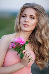 Beautiful pretty woman is wearing fashion dress posing near pink roses in a garden