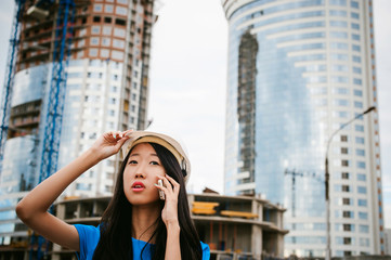 Asian woman in a blue dress and white protective helmet. engineer supervises inspection and control of works at construction site. Business telephone conversations. Communication via smartphone