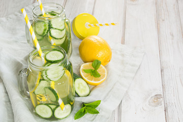 Summer fresh water detox with lemon, cucumber, ice and mint in mason jar on a white wooden background. Rustic style.