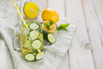 Summer fresh water detox with lemon, cucumber, ice and mint in mason jar on a white wooden background. Rustic style.