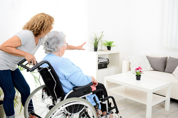Fototapeta na wymiar cheerful mature woman visiting retirement home residence with elderly senior woman on wheelchair