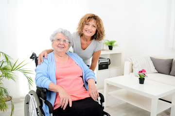 cheerful mature woman visiting retirement home residence with elderly senior woman on wheelchair