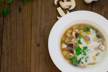Delicious soup with wild mushrooms, potatoes, greens and cream. Wooden background. Top view. Close-up
