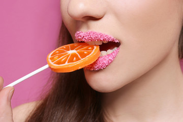 Closeup view of beautiful young woman with sugar lips biting lollipop on color background