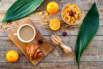 French breakfast. Fresh croissant, coffee, muesli, oranges, cherry on wooden table background top view
