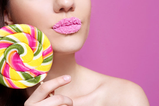 Beautiful young woman holding lollipop near lips covered with sugar on color background, closeup