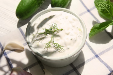 Delicious yogurt sauce in bowl with ingredients on kitchen table