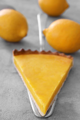 Spatula with piece of delicious lemon pie on gray background