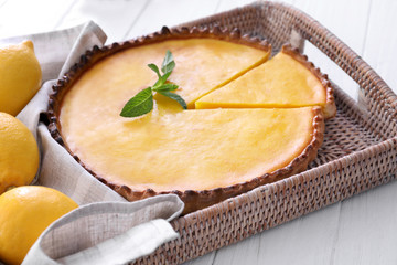 Wicker tray with delicious lemon pie on wooden table, closeup