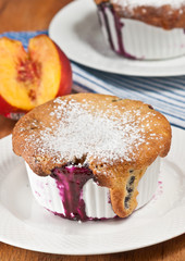 Fresh, baked blueberry-peach cobbler in a cup on a round, white dish with a peach on a blue and white stripped table cloth 