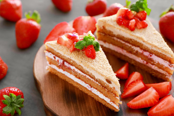 Two pieces of homemade cake with strawberries on wooden board