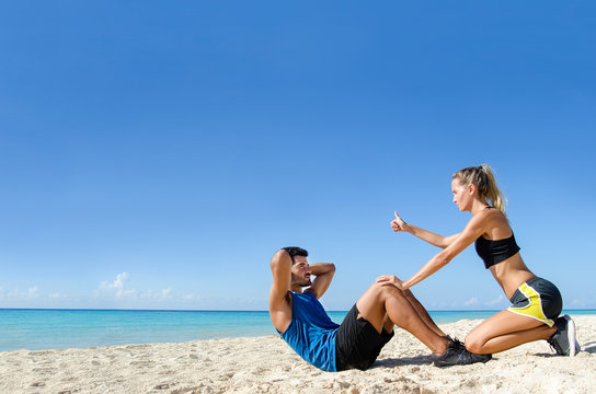 Personal trainer counting crunch at the beach - Powered by Adobe