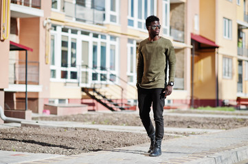 Handsome and attractive african american man in sunglasses posing next to the tall building on a street.