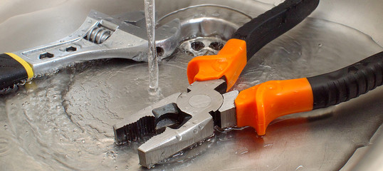 plumbing tools adjustable wrench and pliers in a sink under pouring water, closeup, suitable for...