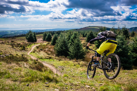 Mountain Biking in Wales - rider speeds down steep flowing trail with river Severn in the background. Cwmcarn, Wales.