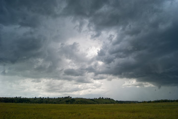 Storm cloud over yellow green fields forests and hills