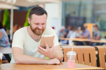 Young man student using a tablet computer in a cafe with a cool drink in the city.