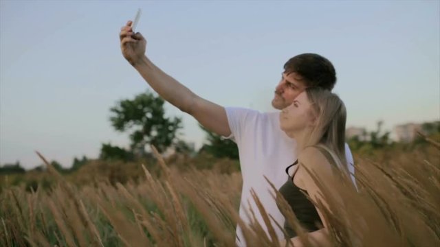 A loving couple, Guy with a beautiful young woman do selfie on the field at the sunset or sunrise