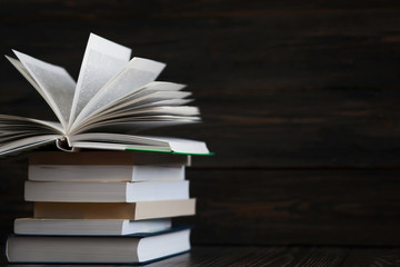  Stack of books with dark wooden background. One book is opened. Free space for text
