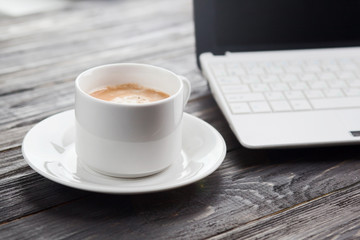 Coffee cup close up and laptop as background on rustic wooden table