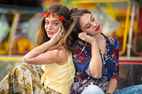 Two teenage girls are listening to music on the headphones