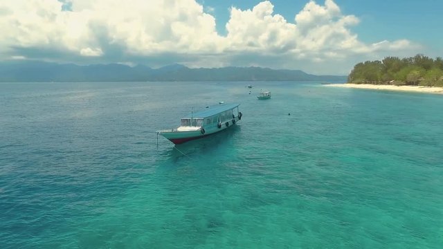 Flying around a boat near Gili Meno Island with perfect turquoise water on a sunny summer day, aerial view with Lombok mountains in background