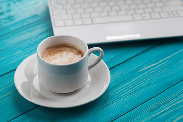 Coffee cup and laptop on the wooden turquoise background, selective focus on coffee cup