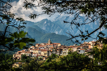 Fototapeta na wymiar Tuscany hilltop village with dramatic mountain backdrop, viewed between trees