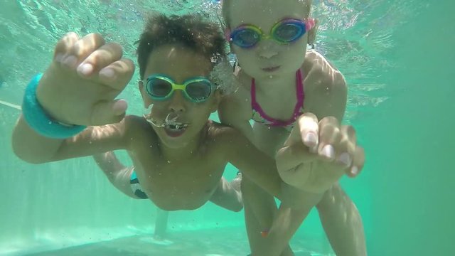 Boy and girl swimming in the pool under water with camera upside down