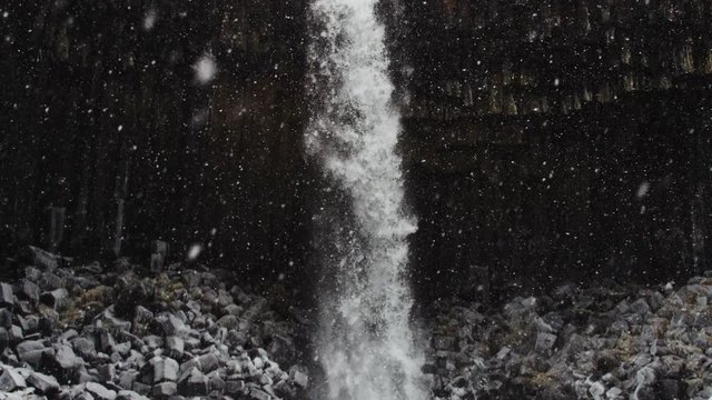 Snow falls over scenic waterfall, tilt down