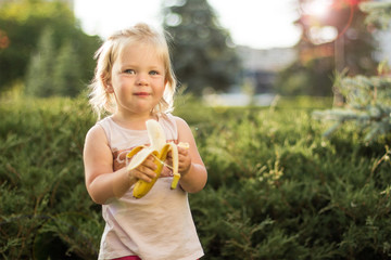 Little girl is eating a banana in the park.