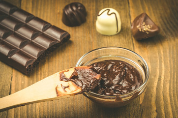 liquid chocolate in a cup and candies/wooden spoon in chocolate on a wooden background
