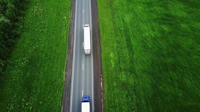 Delivery trucks driving towards the sun. Aerial view f green fields snd trucks